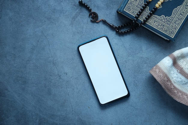 黒の背景にスマートフォンの聖典コーランとロザリオ