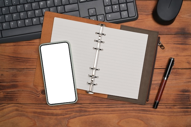 Smart phone, notebook and pen on wooden desk.