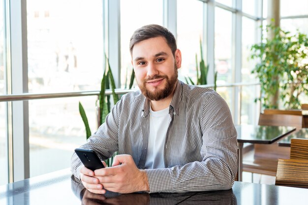 Smart phone sms'en. Aantrekkelijke gebaarde Kaukasische zakenman die smartphone gebruiken terwijl het zitten in bureau. Zakenman, gebruik, gsm, app, in, stedelijke stad, cafe., Man, sms, boodschap, gebruik, smart, phone