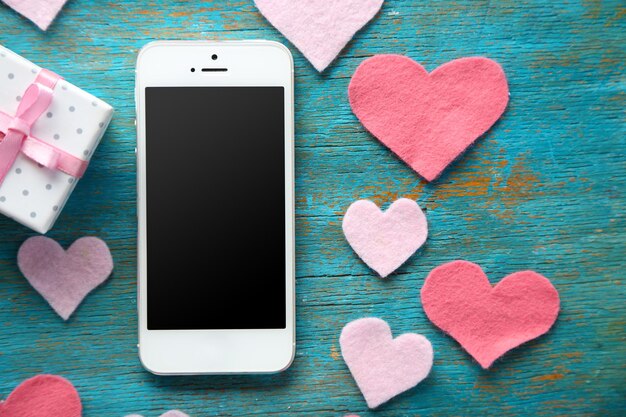 Smart phone with blank screen and hearts on old wooden table