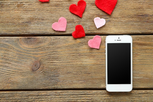 Smart phone with blank screen and hearts on old wooden table