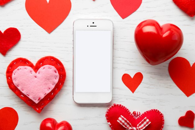 Smart phone with blank screen and hearts on wooden table