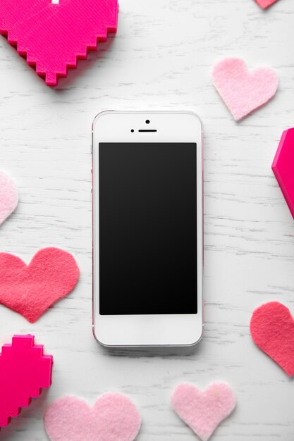 Photo smart phone with blank screen and hearts on wooden table