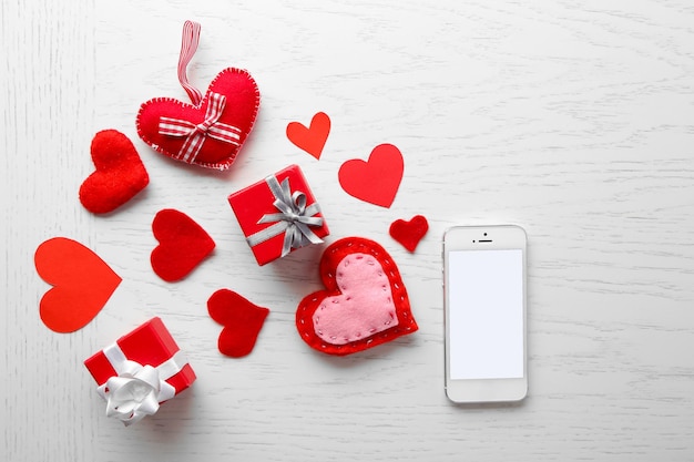 Smart phone with blank screen and hearts on wooden table