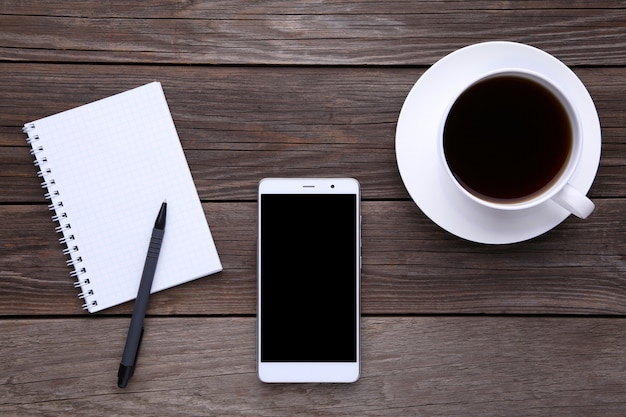 Smart phone with notebook and cup of coffee on grey wooden