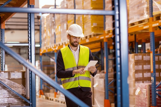smart positive man using a tablet while checking the working process in the warehouse