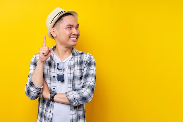 Smart proactive Young handsome ethnic Asian man 20s wearing casual clothes hat pointing finger up at a great new idea looking aside isolated on yellow background studio portrait