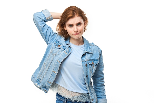 Smart redhead girl in casual touches head thinks doubts makes decision isolated on white studio background