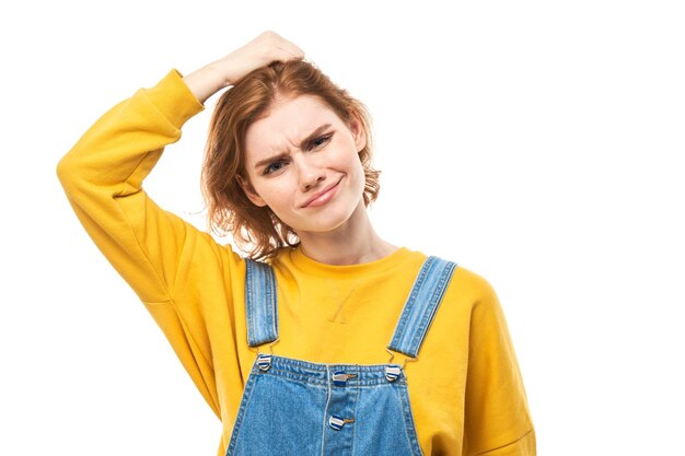 Smart redhead girl in casual touches head thinks doubts makes decision isolated on white studio background