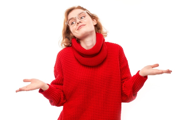 Smart redhead girl in red and glasses shrugging hands thinks doubts makes decision isolated on white studio background