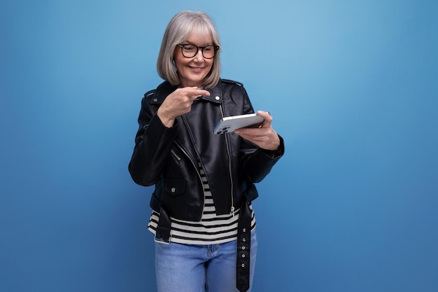 Smart s modern middle aged woman blogger with gray hair with smartphone on bright background