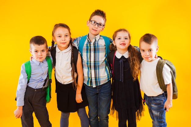 Smart schoolchildren smiling and looking at camera over yellow background Happy kids in school uniform with backpacks Friendship and relationship of classmates