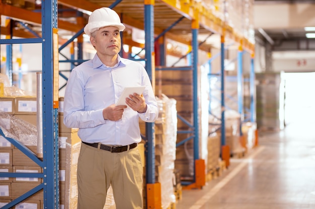 Smart serious manager holding a tablet while controlling the working process