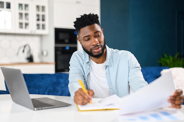 Smart smiling AfricanAmerican male student using laptop for studying online