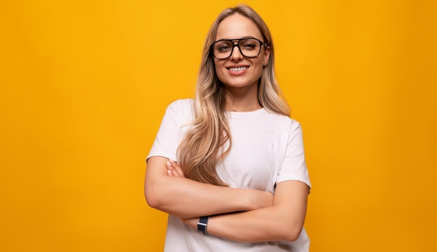 Smart smiling blond woman with poor eyesight wearing glasses on yellow background