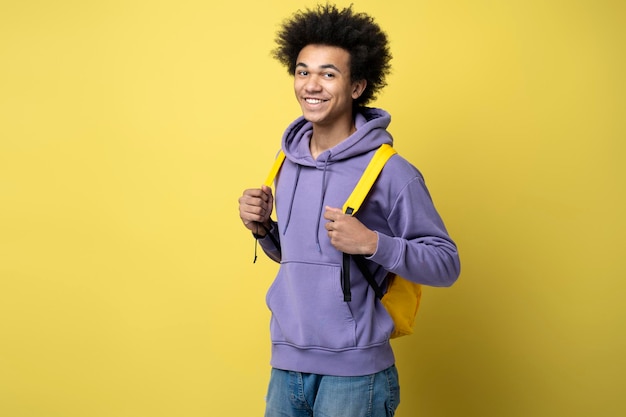 Smart smiling university student with backpack looking at camera isolated on yellow background