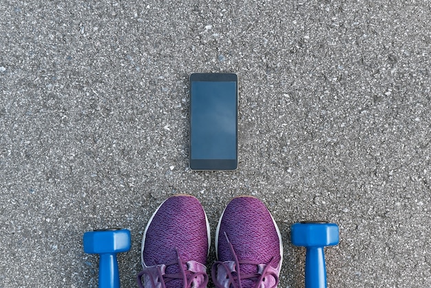 Smart sports gadgets. Cropped photo of dumpbells and purple sneakers at asphalt background. Sport motivation mobile apps
