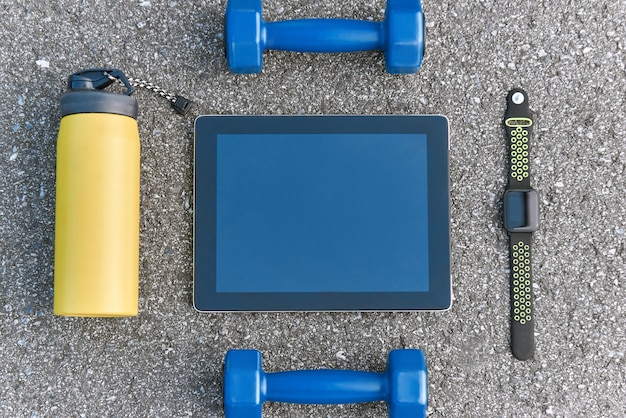 Smart sports gadgets. Cropped photo of dumpbells, water and smart watch at asphalt background. Sport motivation mobile apps