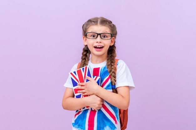 A smart student with glasses holds textbooks on British English in her hands on a pink isolated background.