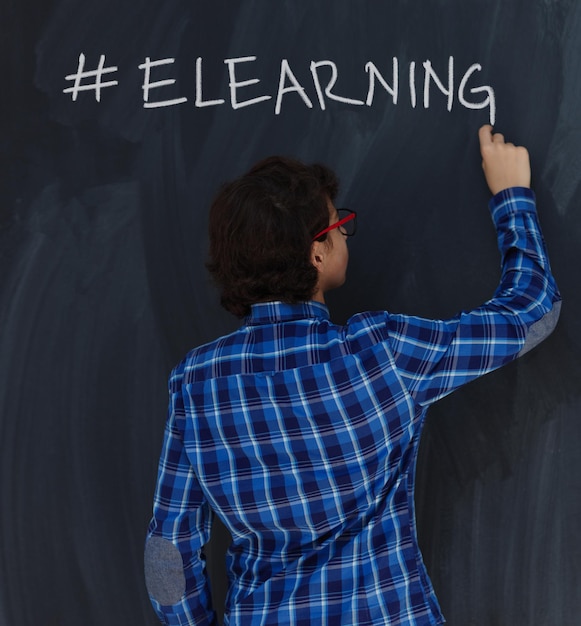Photo smart  teen boy writing with chalk hashtag elearning  on  black board in school coronavirus stay at home concept