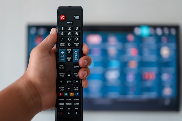 Smart tv e telecomando premendo la mano. mano che tiene il telecomando della tv con un televisore sullo sfondo. avvicinamento.