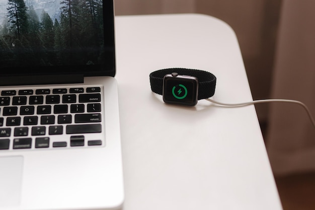 Smart watch on wireless charging with onscreen charging indicator work place near at the laptop