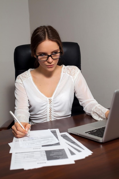 안경을 쓴 똑똑한 여성 상사가 노트북을 사용하여 서류 작업을 하고 있습니다