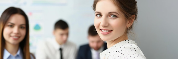 Smart woman sitting in big modern office with colleagues and smile at camera