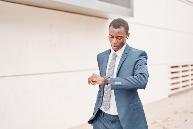 Smart young AfricanAmerican businessman in a modern suit looking at his watch walking in the background of the city