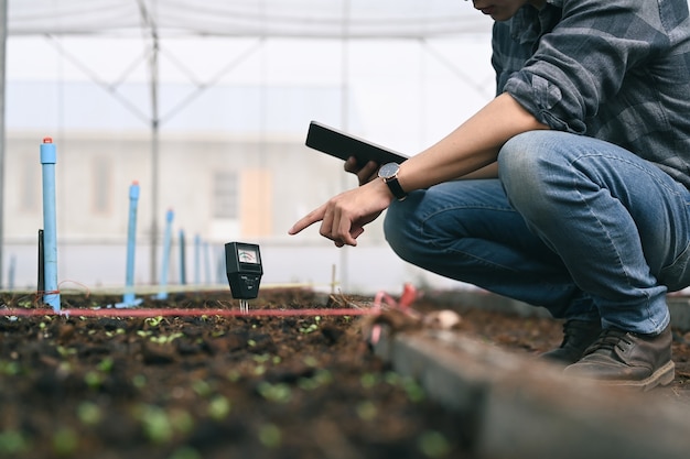 Smart young asian agronomist man measure soil with digital device and tablet. Technology in the agriculture.