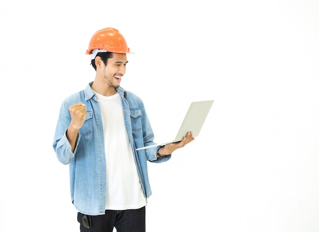 스마트 젊은 아시아 건축가 엔지니어 남자 행복과 성공 위치와 그의 계획된 작업을 확인하기 위해 노트북을 들고 손 캐주얼 진 오렌지 안전 헬멧을 착용