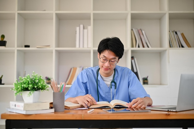 写真 制服を着た賢い若いアジア人男性医学生が本を読むことに集中している