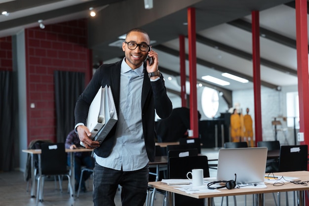 Photo smart young businnessman talking on the smartphone and carrying folders in the office