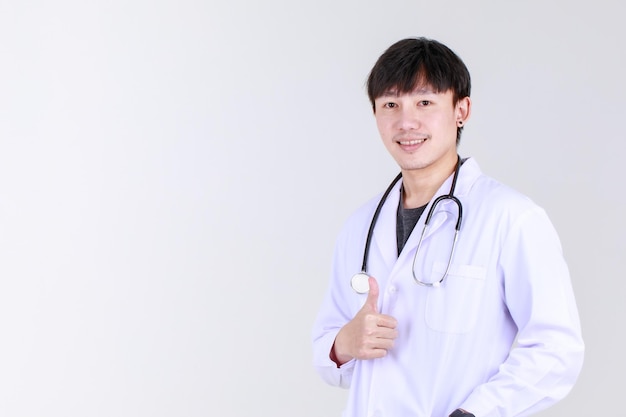 의료 전문 가운을 입은 똑똑한 젊은 중국 의사는 청진기 미소와 엄지손가락을 위로 올려 안전하고 성공적인 질병 치료에 만족합니다