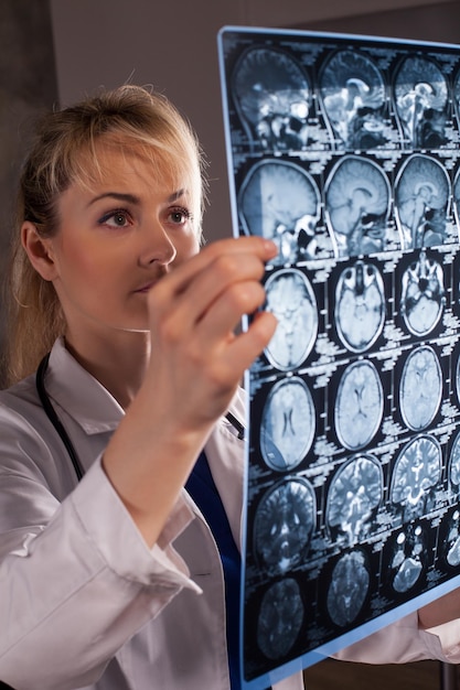 Smart young doctor woman in white labcoat looking through mri of human brain