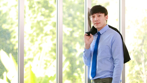 Smart young executive businessman on formal working suit and elegant neck tie standing confidently at company office and carrying jacket ready to enjoy lifestyle of corporate management in summer