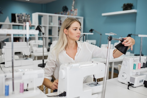 A smartlooking woman is sewing with the electric sewingmachine Fashion tailors workshop