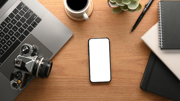 Smartphone blank screen mockup on wooden worktable with digital devices and decorations. top view