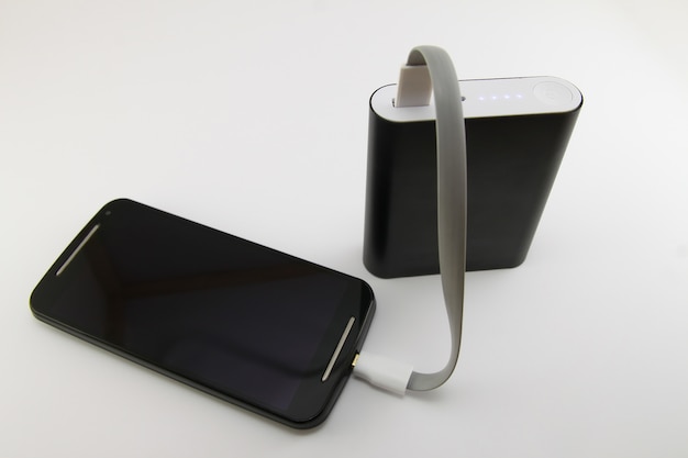 Smartphone che si carica dalla banca di potere nera isolata su bianco. concetto di smartphone e power bank.