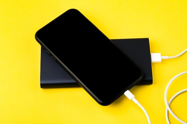 Smartphone charging with power Bank via USB cable on yellow background top view