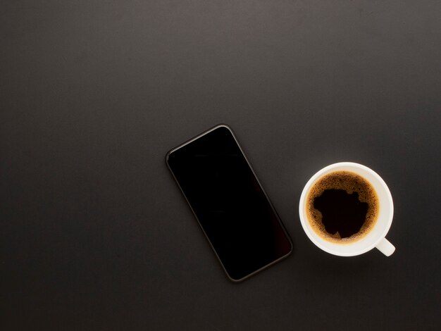 Smartphone and coffee on black background.