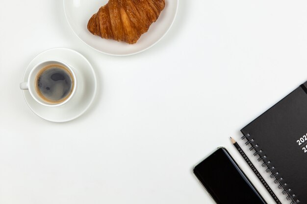 Smartphone, coffee, notebook, pencil and croissant