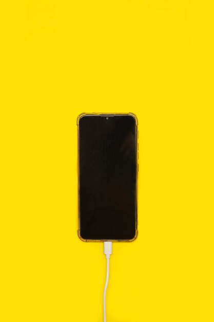 黄色い背景の充電ケーブルに接続されたスマートフォン