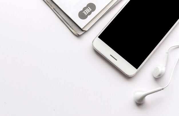 Smartphone, earphone and magazine on  white table with over light in the background