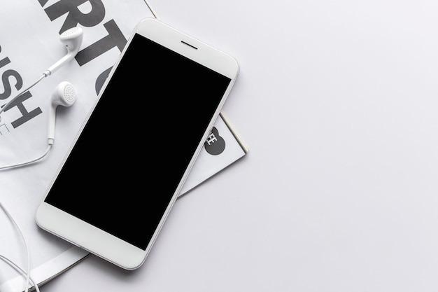 Smartphone, earphone and magazine on  white table with over light in the background