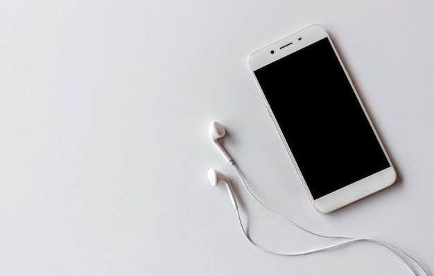 Smartphone and earphone on white table with over light in the background