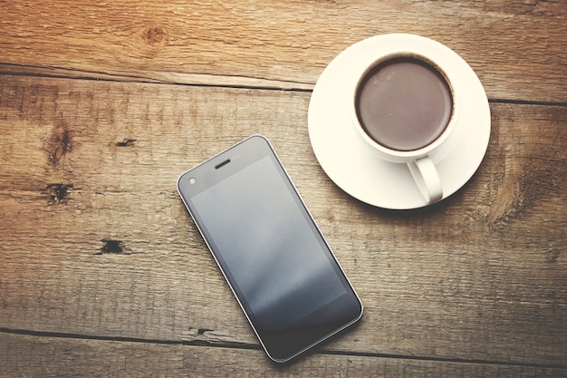 smartphone en koffiekopje op een houten tafel