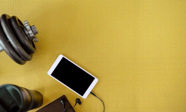 Smartphone and fitness equipment on yellow mat.