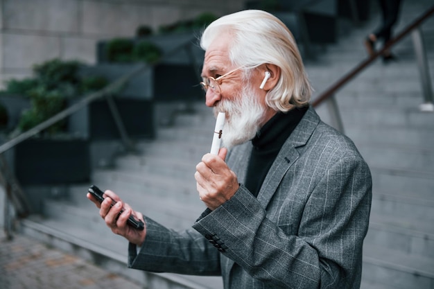 Smartphone gebruiken Senior zakenman in formele kleding met grijs haar en baard is buitenshuis