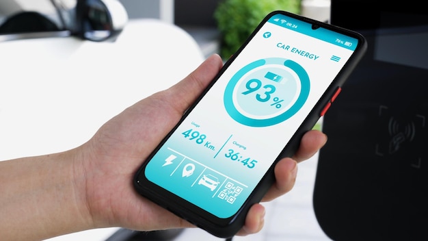 Smartphone geeft de batterijstatus weer op een slimme mobiele EV-applicatie terwijl de EV-auto elektriciteit oplaadt via een thuislaadstation in de garage Toekomstige innovatieve EV-auto en energieduurzaamheid Doorlezen